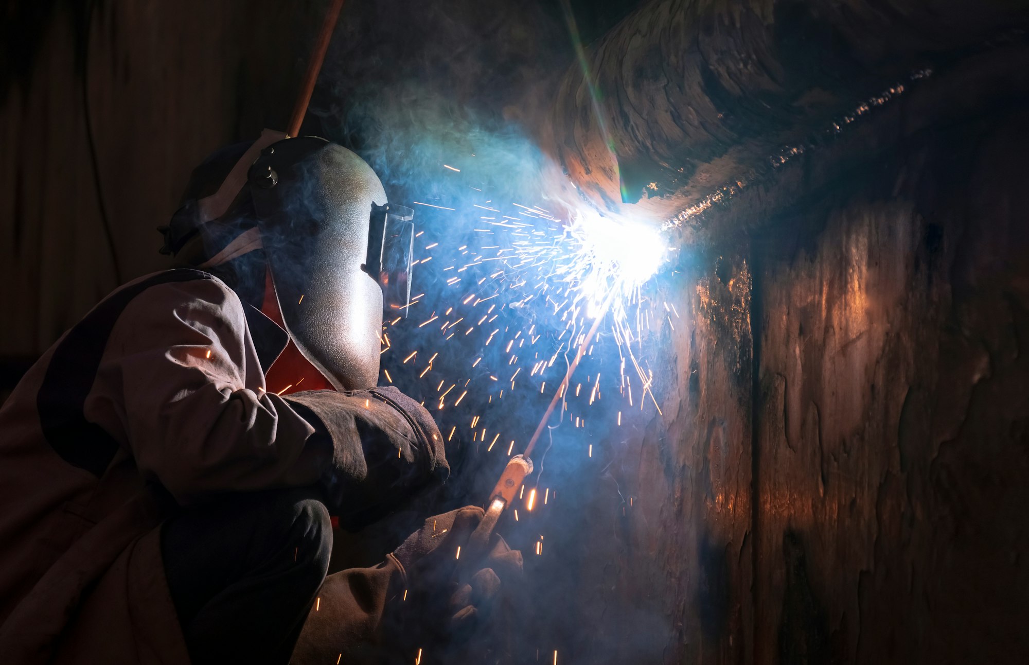 welder using arc welding machine to welding metal wall of the old vessel at shipyard in dark tone